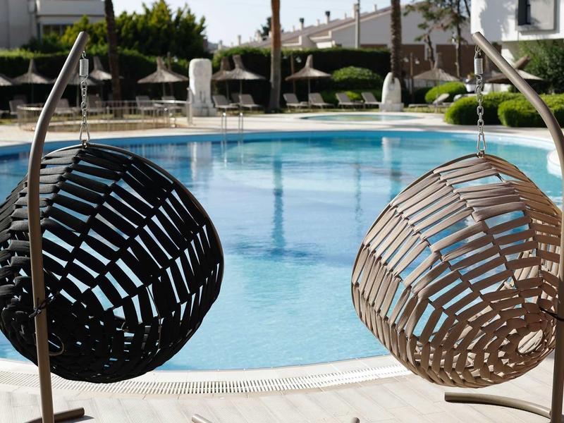 Twee hangstoelen naast een rond zwembad in een buitenruimte van een hotel.