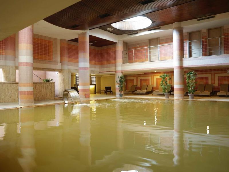 Groot binnenzwembad met zuilen en decoratieve muurschilderingen in een stijlvolle spa.