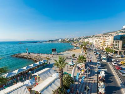 Küstenpromenade mit Palmen, Strand und mehrstöckigen Gebäuden bei klarem Himmel