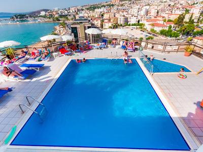 Großer blauer Pool mit Liegestühlen und Meerblick in einer Küstenstadt.