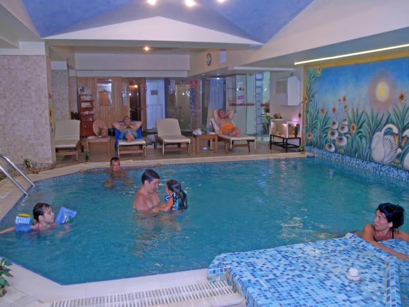 Kryty basen hotelowy z gośćmi odpoczywającymi w wodzie i siedzącymi obok.