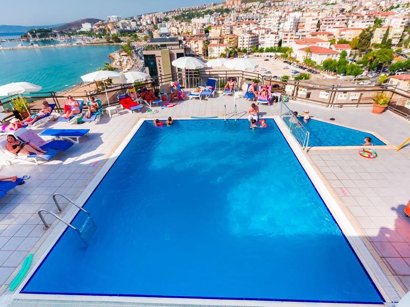 Trzy baseny z leżakami w hotelu z widokiem na morze i miasto.