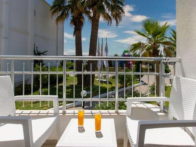 Balkon mit zwei weißen Stühlen und Getränken, Palmen und Meer im Hintergrund.