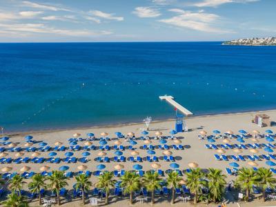 Ampia spiaggia sabbiosa con ombrelloni blu e lettini vicino al mare blu calmo.