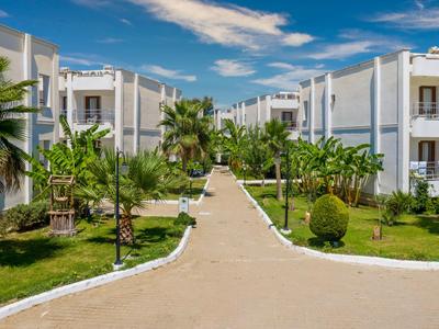 Hotelanlage mit weißen Gebäuden, grünem Garten und gepflastertem Weg unter blauem Himmel.