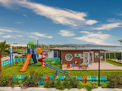 Parco giochi colorato per bambini davanti a un hotel con palme e vista sulle montagne.