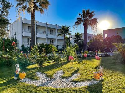 Hotel mit Garten voller Palmen, Blumen und Flamingos bei Sonnenuntergang