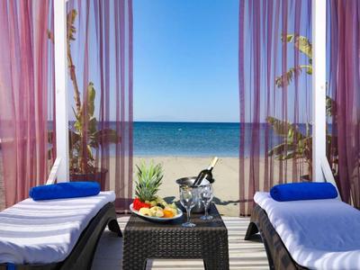 Strandblick von einer Terrasse mit zwei Liegestühlen, blauem Handtuch und einem Tisch mit Obst und Wein.