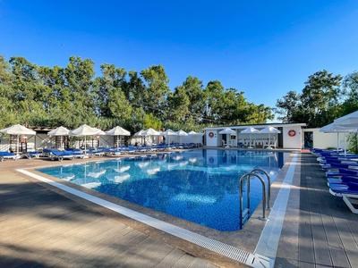 Großer Swimmingpool mit Liegestühlen und Sonnenschirmen neben Bäumen und klarem Himmel.