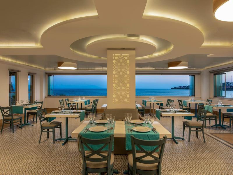 Ristorante moderno con vista mare e illuminazione elegante al crepuscolo.
