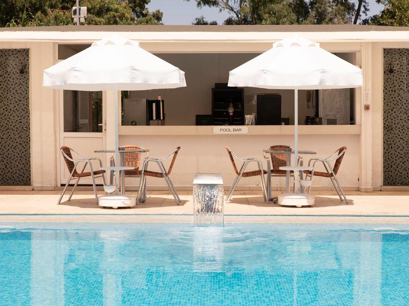 Zona piscina con due ombrelloni bianchi e sedie davanti a un bar all'aperto.