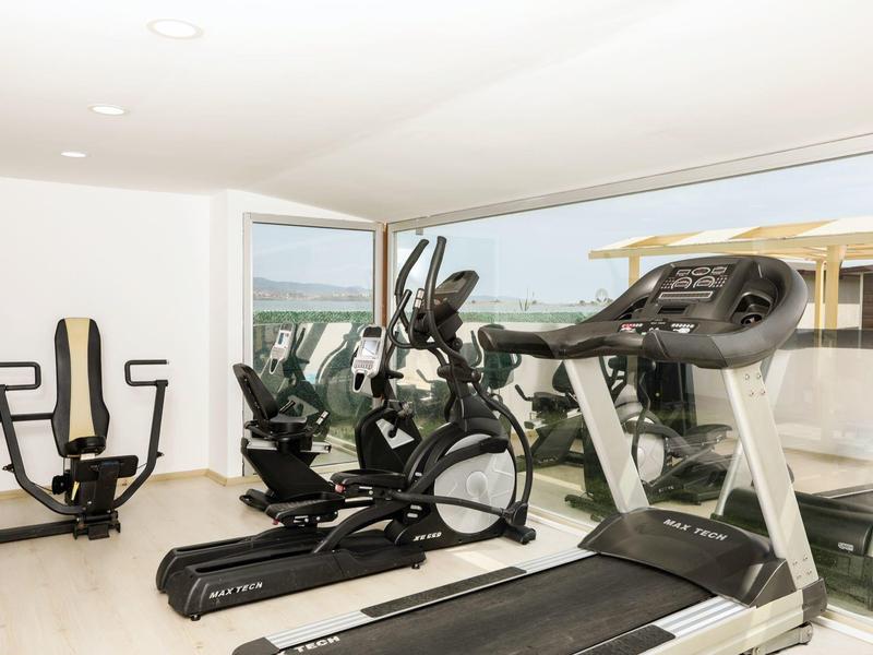 Palestra luminosa con tapis roulant, ellittica e macchina per esercizi con grande finestra e vista sul mare.