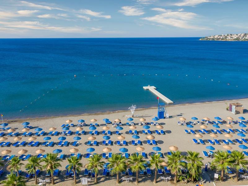 Ampia spiaggia sabbiosa con ombrelloni blu e lettini vicino al mare blu calmo.