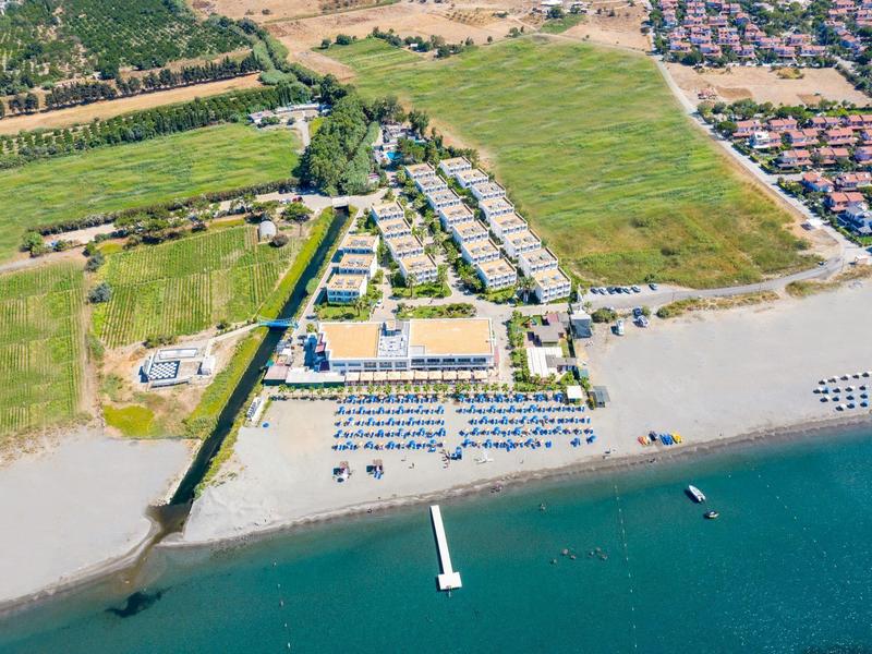 Veduta aerea di una spiaggia con ombrelloni, lettini e resort adiacente vicino a una zona residenziale.