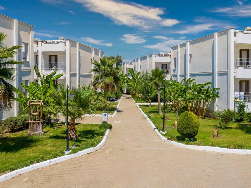 Viale tra edifici bianchi dell'hotel con palme e prato verde sotto cielo blu.