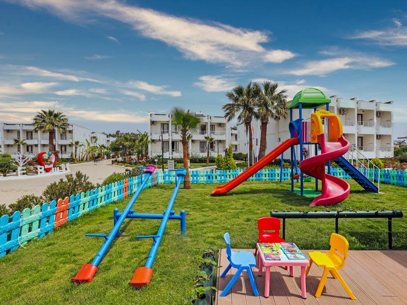 Parco giochi colorato con scivoli e altalene in un giardino d'hotel con palme.