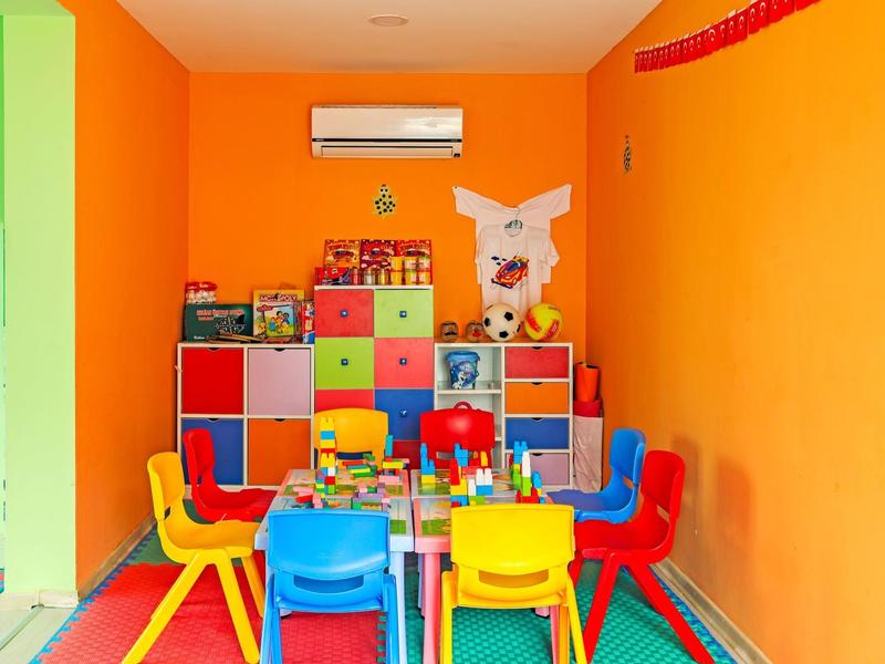 Sala giochi colorata per bambini con tavoli, sedie e armadio in una stanza arancione.
