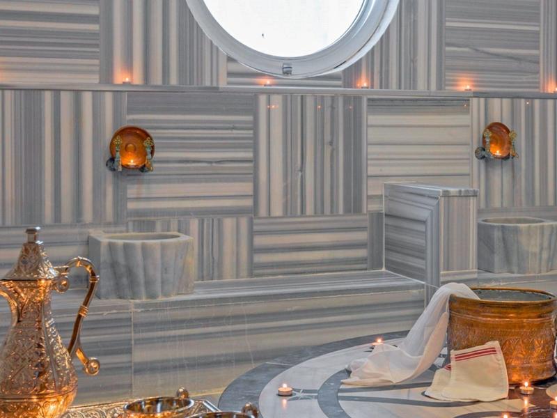 Teiere e tazze tradizionali su un tavolo davanti a una parete artisticamente decorata con motivo orientale.