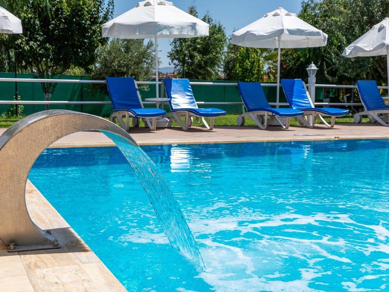 Piscina con elemento d'acqua e lettini blu sotto ombrelloni bianchi