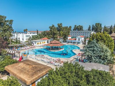 Schwimmbad mit großer blauer Wasserfläche, umgeben von Liegestühlen, Bäumen und Gebäuden.