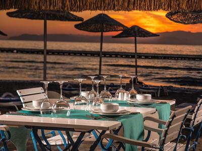 Tisch mit gedecktem Geschirr am Strand bei Sonnenuntergang und Schirmen.