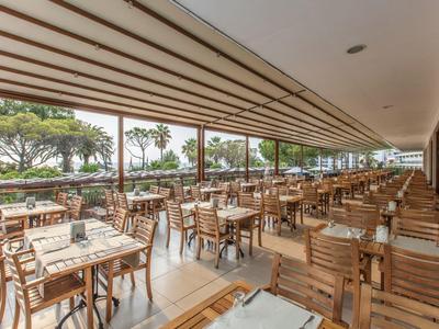 Terrasse de restaurant avec tables en bois et vue sur jardin verdoyant et palmiers.