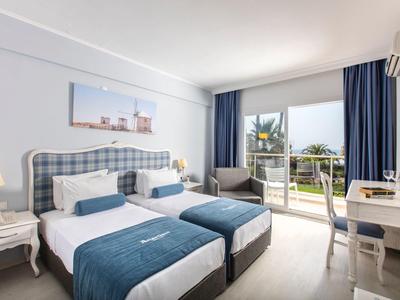 Chambre d'hôtel lumineuse avec lits jumeaux et vue sur jardin depuis la terrasse.