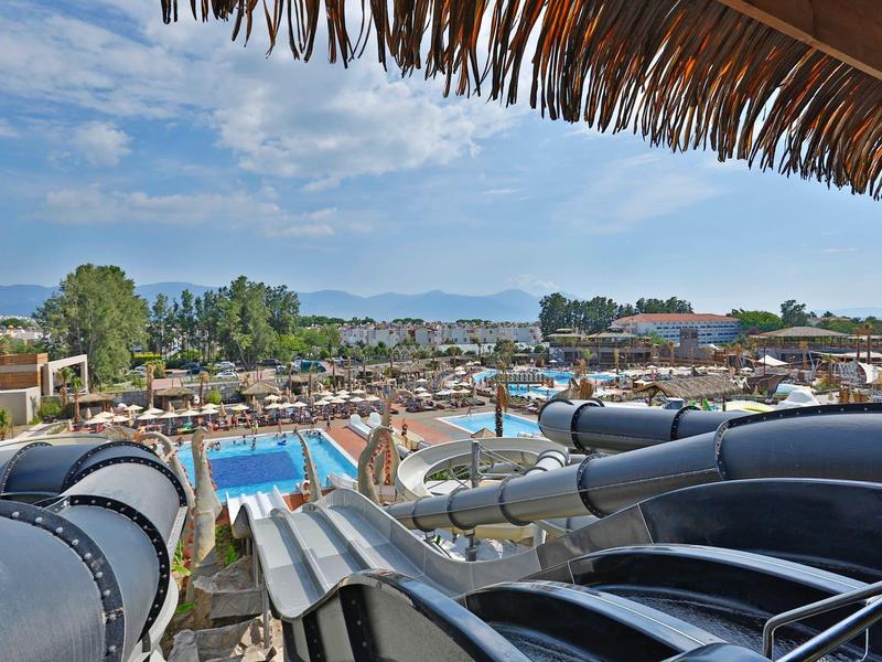 Vue d'un parc aquatique avec toboggans noirs et piscine sous un ciel bleu.