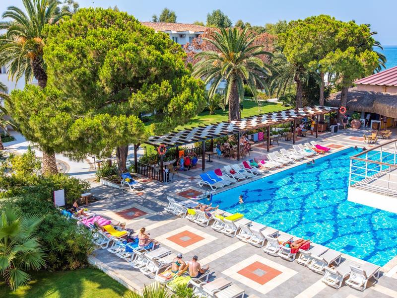 Piscine d'hôtel entourée de chaises longues et de grands arbres verts.