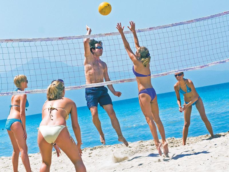 Des personnes jouent au volley-ball sur une plage ensoleillée avec un filet et la mer en arrière-plan.