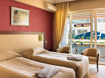 Hotelzimmer mit zwei Einzelbetten, Sessel und Fenster mit Blick auf Terrasse und Sonnenschirm.
