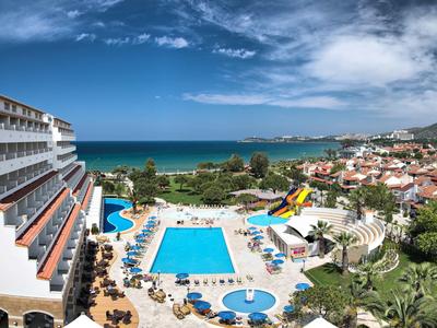 Hotel mit großen Pools und Terrasse nahe am Meer unter blauem Himmel.