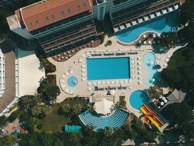 Vogelperspektive eines Hotels mit mehreren Pools, Sonnenterrassen und angrenzendem Wald.