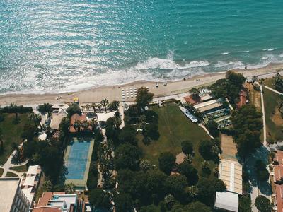 Vogelperspektive eines Strandes mit klarem Wasser, Hotels und grünen Gartenanlagen.