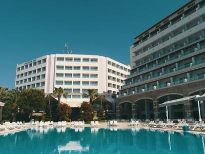 Modernes Hotel mit großem Pool und Liegestühlen unter blauem Himmel.