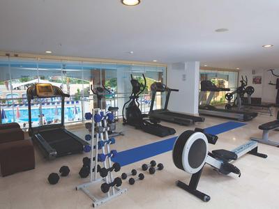 Innenraum eines modernen Fitnessstudios mit Laufbändern, Rudergerät und Hanteln vor großen Fenstern.