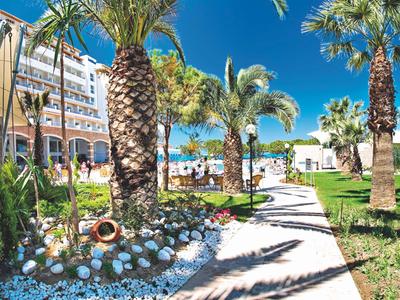 Sonniger Hotelweg mit Palmen, blauer Himmel und Blick auf den Strand am Meer.