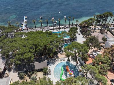 Luftaufnahme von Meer, Palmen und mehreren Pools in einem tropischen Resort bei sonnigem Wetter.
