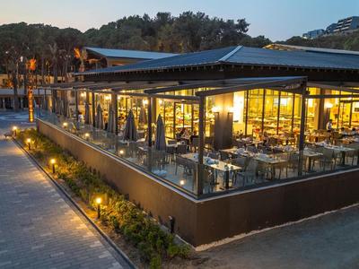 Moderner, beleuchteter Außenbereich eines Restaurants bei Abenddämmerung mit Sitzplätzen und Pflanzen.