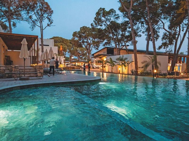 Oświetlony basen o zmierzchu z drzewami i budynkami w tle.