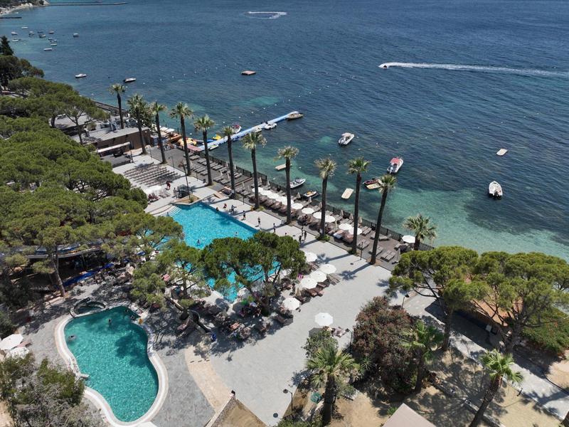 Widok na basen hotelowy z palmami wzdłuż wybrzeża i łodziami na morzu w słoneczny dzień.