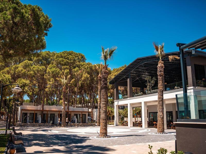 Nowoczesny kompleks hotelowy z palmami i sosnami pod jasnym niebem.