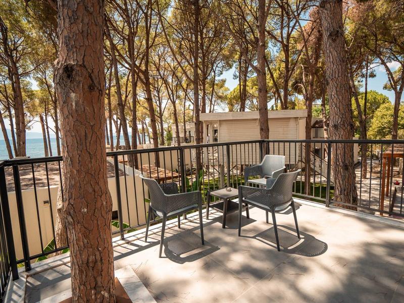 Balkon z krzesłami i stołem otoczony drzewami, widok na budynki i morze.