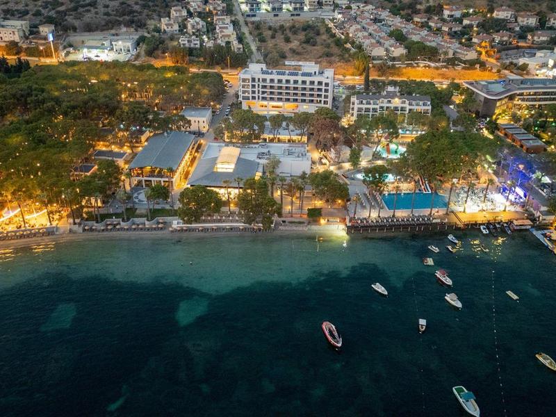 Nocne zdjęcie z lotu ptaka oświetlonego kurortu nad morzem z łodziami na wodzie.