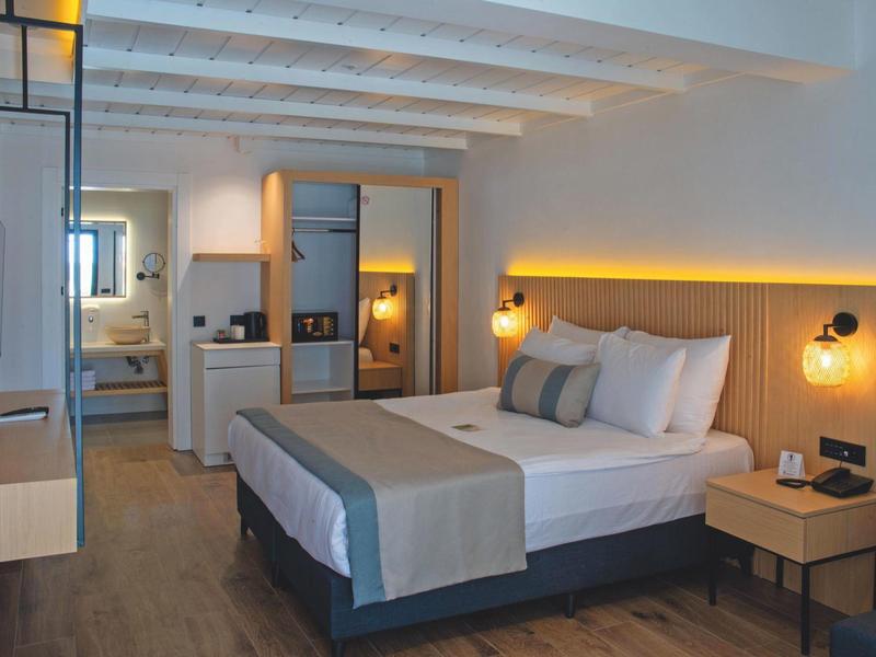 Nowoczesny pokój hotelowy z łóżkiem podwójnym, drewnianymi elementami i oświetleniem pośrednim.