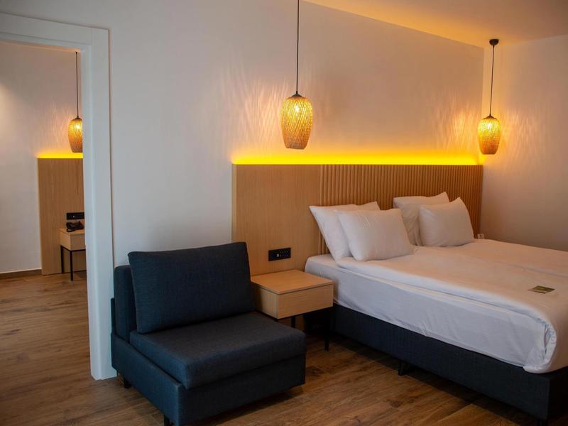 Nowoczesny pokój hotelowy z podwójnym łóżkiem, stolikami nocnymi, fotelem i ciepłym światłem.