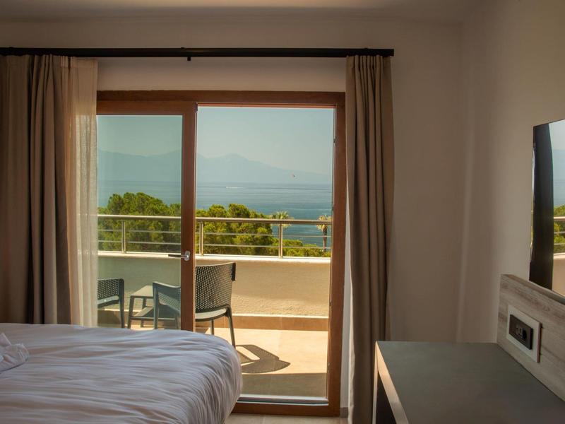 Widok z sypialni na balkon z krzesłami i morze w tle.