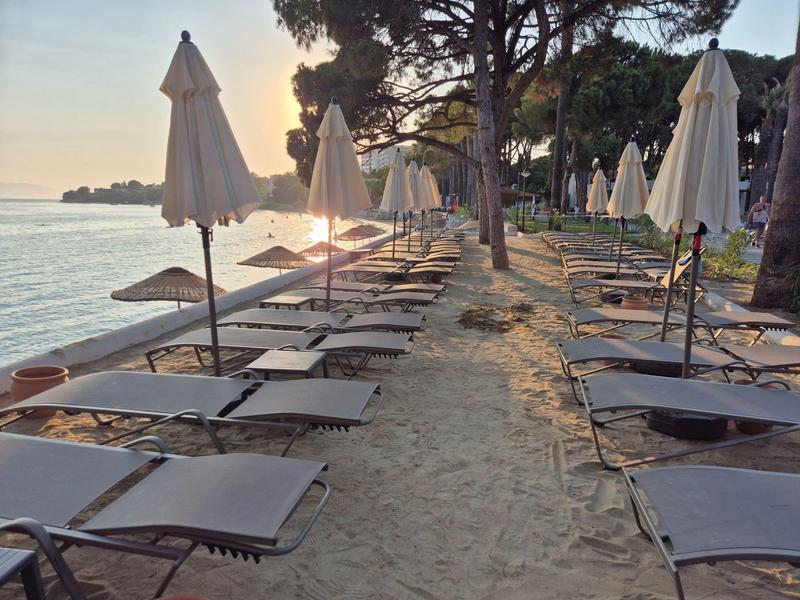 Plaża z leżakami i zamkniętymi parasolami o zachodzie słońca.