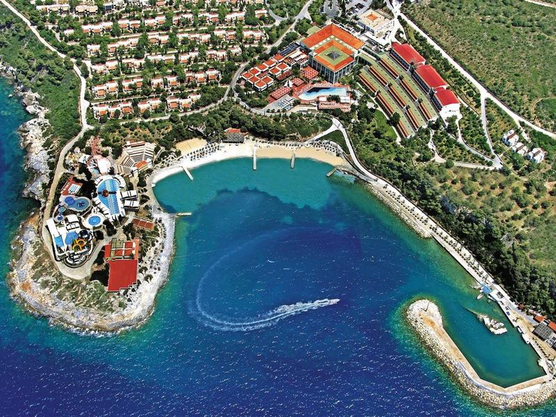 Aerial view of a coastal resort with hotel facilities, pools, and marina by the sea