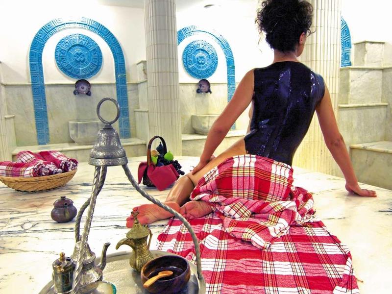 Woman sitting on marble floor in traditional Turkish bath with red tiles.